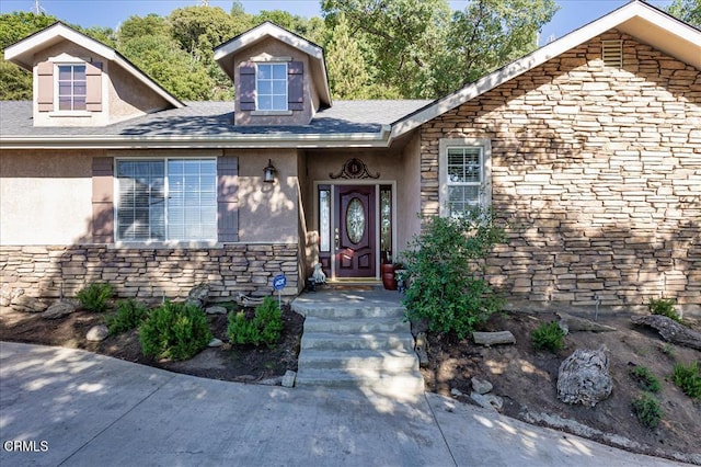 doorway to property with stone siding, a shingled roof, and stucco siding