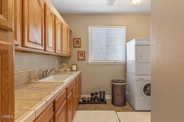 clothes washing area with cabinet space, stacked washing maching and dryer, tile patterned flooring, and a sink