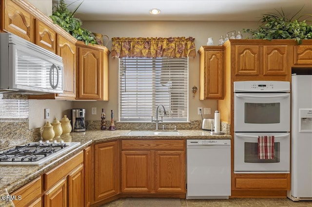 kitchen featuring a sink, brown cabinets, white appliances, and recessed lighting