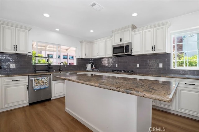 kitchen with white cabinetry, stainless steel appliances, backsplash, and wood finished floors