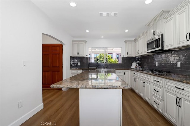 kitchen featuring dark wood-style flooring, decorative backsplash, visible vents, light stone counters, and appliances with stainless steel finishes