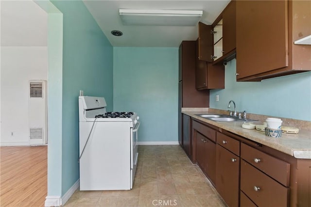 kitchen featuring a heating unit, a sink, light countertops, baseboards, and gas range gas stove