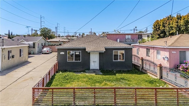 bungalow featuring a front lawn, a shingled roof, a residential view, fence private yard, and stucco siding