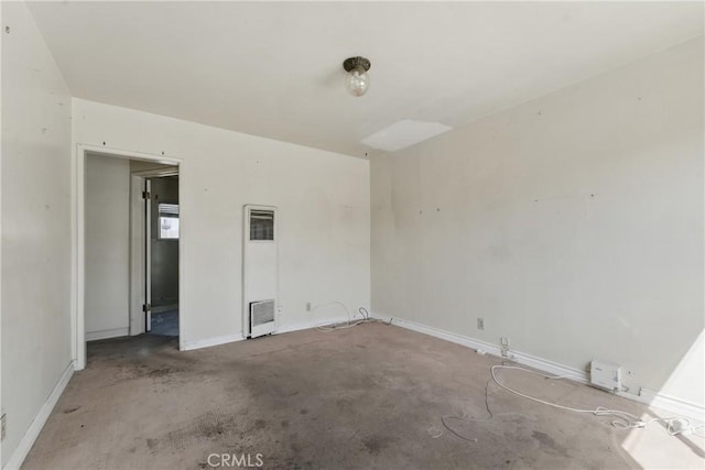 empty room featuring a heating unit, unfinished concrete flooring, and baseboards