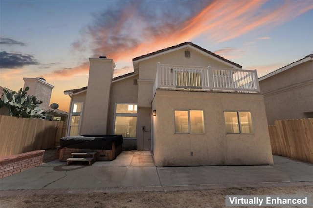 back of house with stucco siding, a fenced backyard, a balcony, and a hot tub