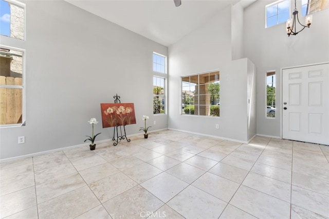 tiled foyer with a wealth of natural light, a chandelier, high vaulted ceiling, and baseboards