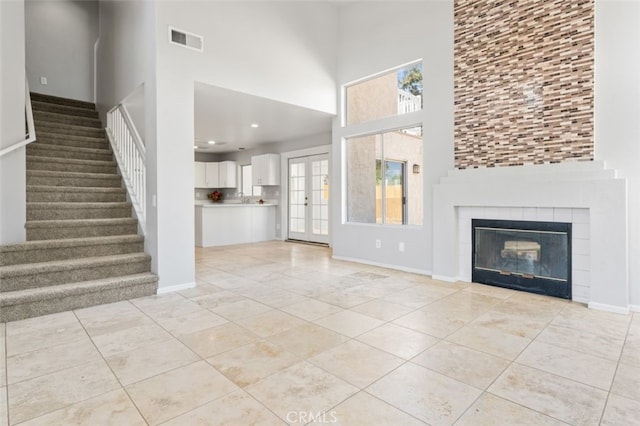 unfurnished living room with stairway, visible vents, baseboards, and a high ceiling