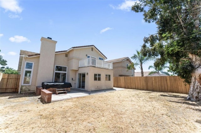 rear view of property with a balcony, a chimney, a patio area, a hot tub, and a fenced backyard