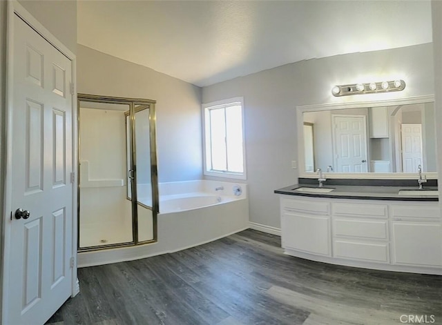 bathroom with a sink, double vanity, a bath, and wood finished floors
