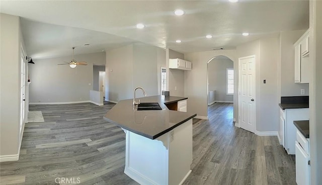 kitchen with ceiling fan, dark countertops, a sink, arched walkways, and wood finished floors