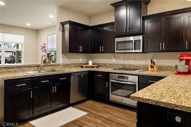 kitchen featuring wood finished floors, a sink, light stone counters, a peninsula, and stainless steel appliances