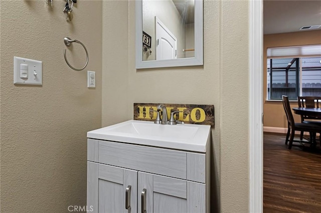 bathroom with a textured wall, vanity, baseboards, wood finished floors, and visible vents