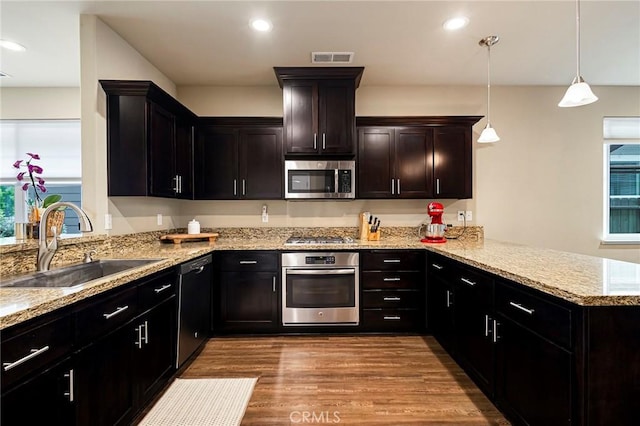 kitchen with light stone counters, a sink, stainless steel appliances, a peninsula, and wood finished floors