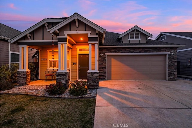 craftsman-style house featuring a garage, covered porch, stone siding, and concrete driveway
