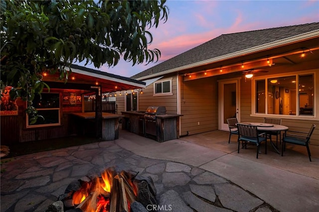 back of house at dusk with a patio, a shingled roof, a fire pit, and area for grilling