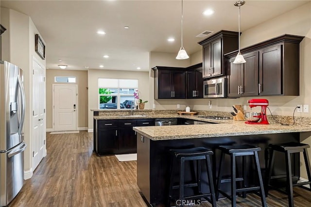 kitchen with dark brown cabinets, appliances with stainless steel finishes, a peninsula, decorative light fixtures, and dark wood-type flooring