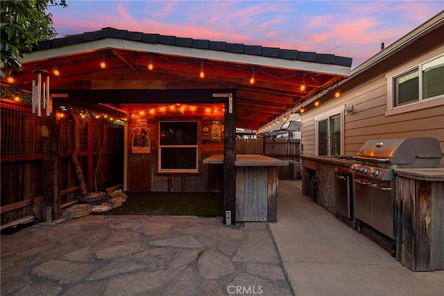 patio terrace at dusk featuring area for grilling, fence, and outdoor dry bar