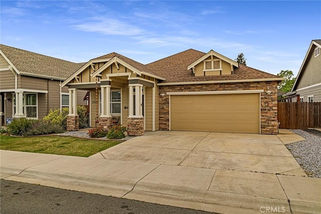 craftsman-style house featuring a front yard, a garage, fence, concrete driveway, and stone siding