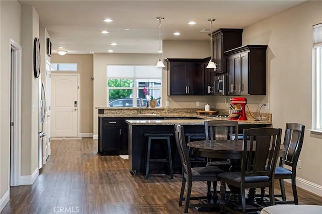 kitchen featuring a peninsula, dark brown cabinets, light stone countertops, baseboards, and dark wood finished floors