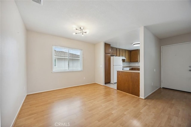 kitchen with light wood-style floors, brown cabinets, freestanding refrigerator, and baseboards