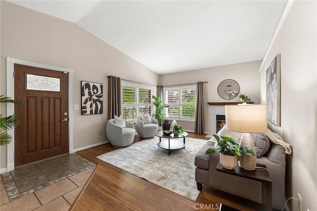 living room with wood finished floors, a premium fireplace, vaulted ceiling, and baseboards