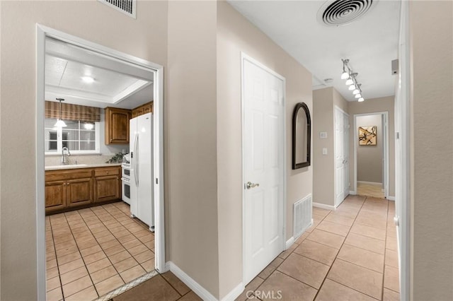 hallway featuring light tile patterned floors, visible vents, a tray ceiling, and a sink