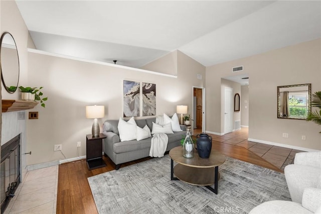 living area with vaulted ceiling, light wood-type flooring, a fireplace, baseboards, and visible vents