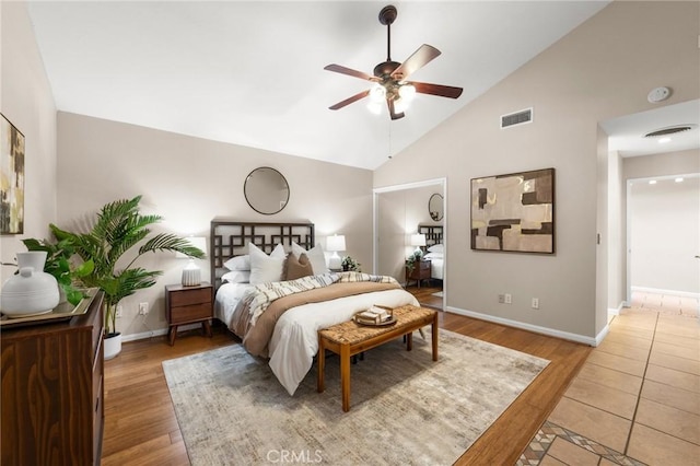 bedroom with ceiling fan, visible vents, baseboards, light wood-type flooring, and high vaulted ceiling