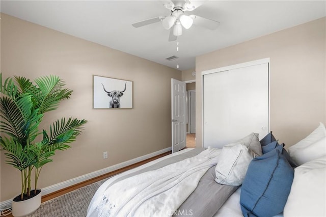 bedroom with visible vents, a closet, baseboards, wood finished floors, and a ceiling fan