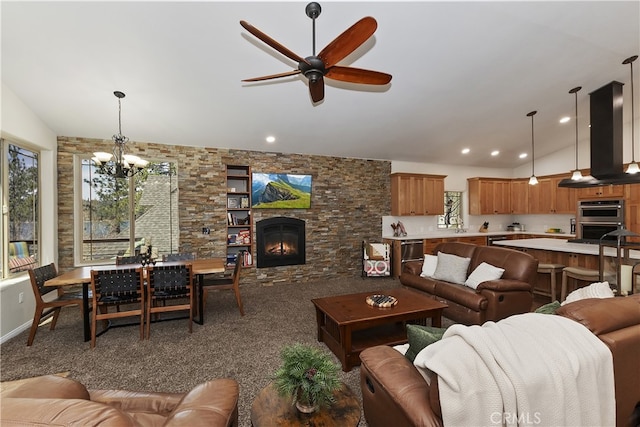carpeted living room with ceiling fan with notable chandelier, plenty of natural light, a fireplace, and vaulted ceiling