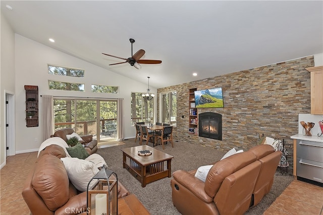 living room with light tile patterned floors, ceiling fan with notable chandelier, a stone fireplace, baseboards, and high vaulted ceiling