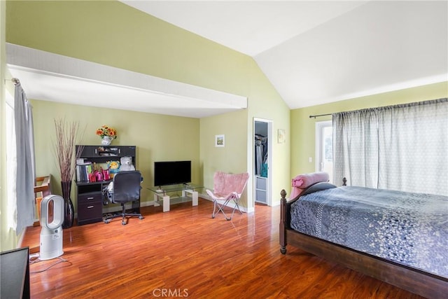 bedroom with baseboards, vaulted ceiling, wood finished floors, and a walk in closet
