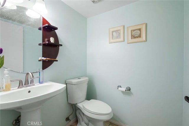half bathroom featuring toilet, baseboards, and a sink