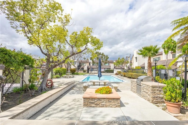 community pool with a patio area, fence, a residential view, and an outdoor kitchen