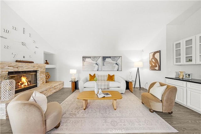 living room featuring built in shelves, dark wood-style flooring, a stone fireplace, and lofted ceiling
