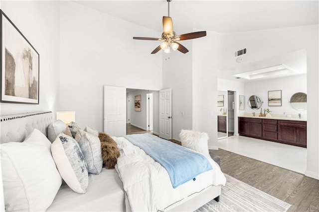 bedroom featuring visible vents, wood finished floors, high vaulted ceiling, baseboards, and connected bathroom