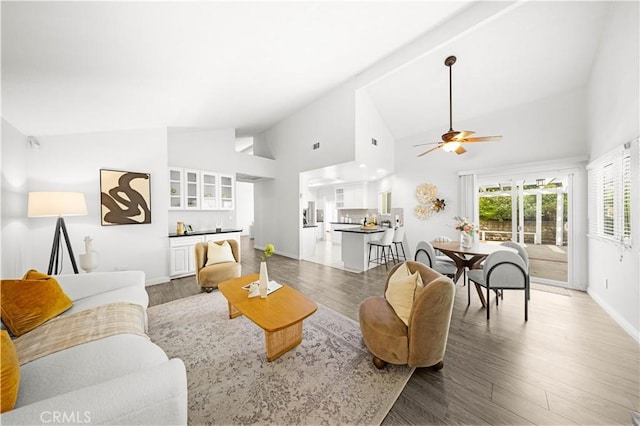 living area with baseboards, ceiling fan, wood finished floors, and high vaulted ceiling