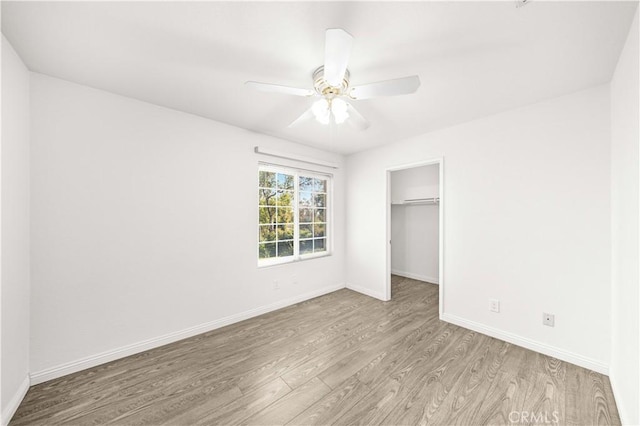 unfurnished bedroom featuring a ceiling fan, wood finished floors, baseboards, a closet, and a spacious closet