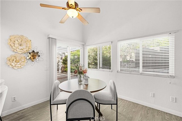 dining area featuring baseboards, ceiling fan, a high ceiling, and light wood-type flooring