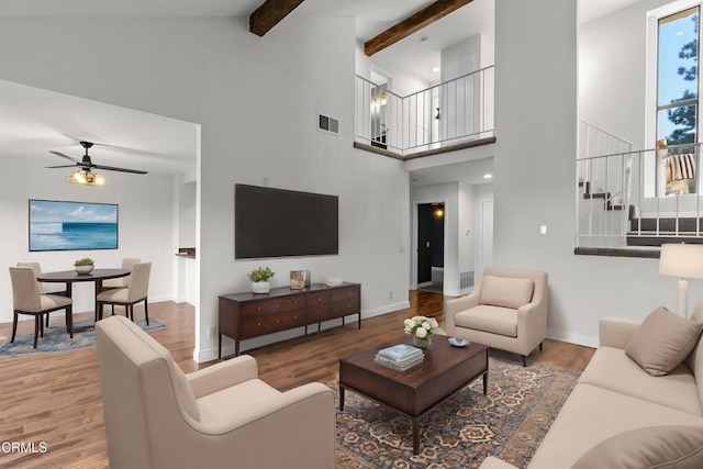 living room with wood finished floors, stairs, ceiling fan, visible vents, and a high ceiling