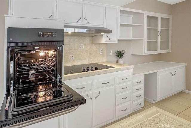 kitchen with black appliances, white cabinets, under cabinet range hood, and decorative backsplash