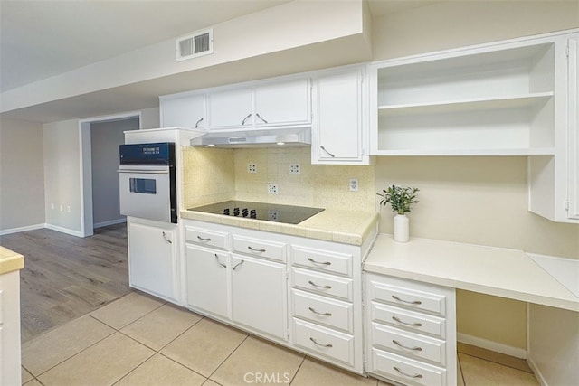 kitchen with black electric stovetop, white cabinets, visible vents, under cabinet range hood, and white oven