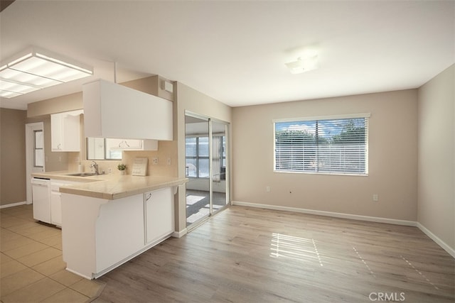 kitchen featuring baseboards, white cabinets, dishwasher, and light countertops