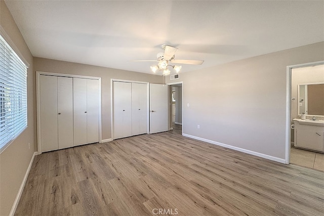unfurnished bedroom with baseboards, visible vents, light wood-style floors, and two closets