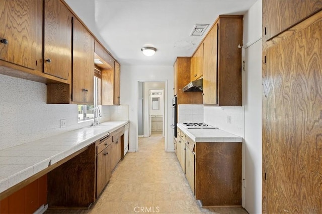 kitchen featuring under cabinet range hood, light countertops, backsplash, and visible vents