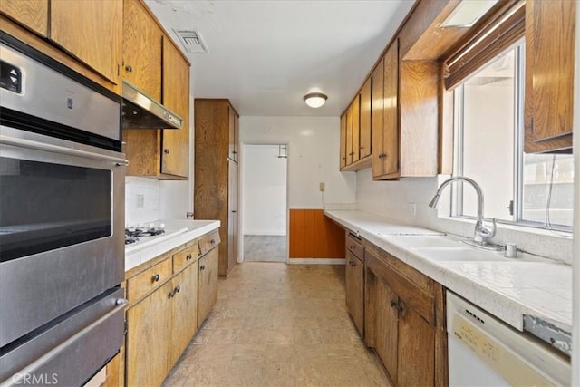 kitchen featuring a sink, white appliances, brown cabinetry, visible vents, and a warming drawer