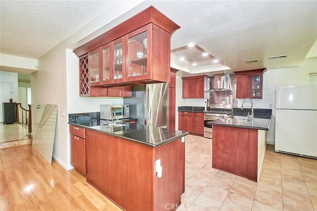 kitchen with wall chimney range hood, appliances with stainless steel finishes, a sink, a textured ceiling, and a peninsula