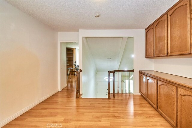 corridor with baseboards, a textured ceiling, light wood-style flooring, and an upstairs landing