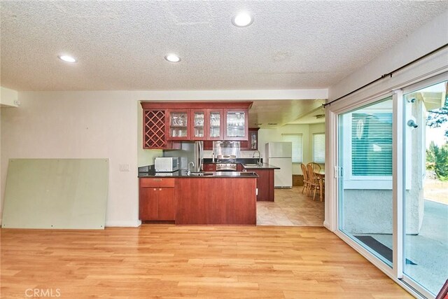 kitchen featuring dark countertops, white appliances, a textured ceiling, light wood-style flooring, and a peninsula