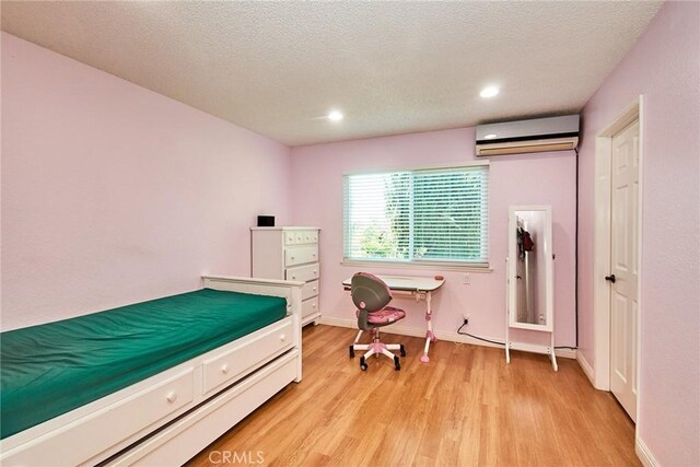 bedroom with light wood-style floors, baseboards, recessed lighting, a textured ceiling, and a wall unit AC